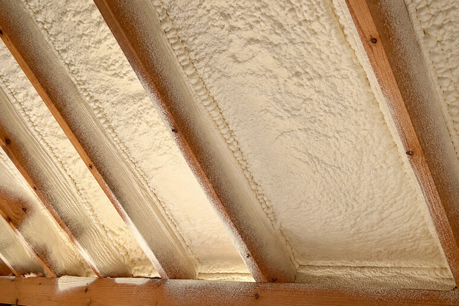 Cream-colored spray foam fills the roof bays between exposed wooden rafters.