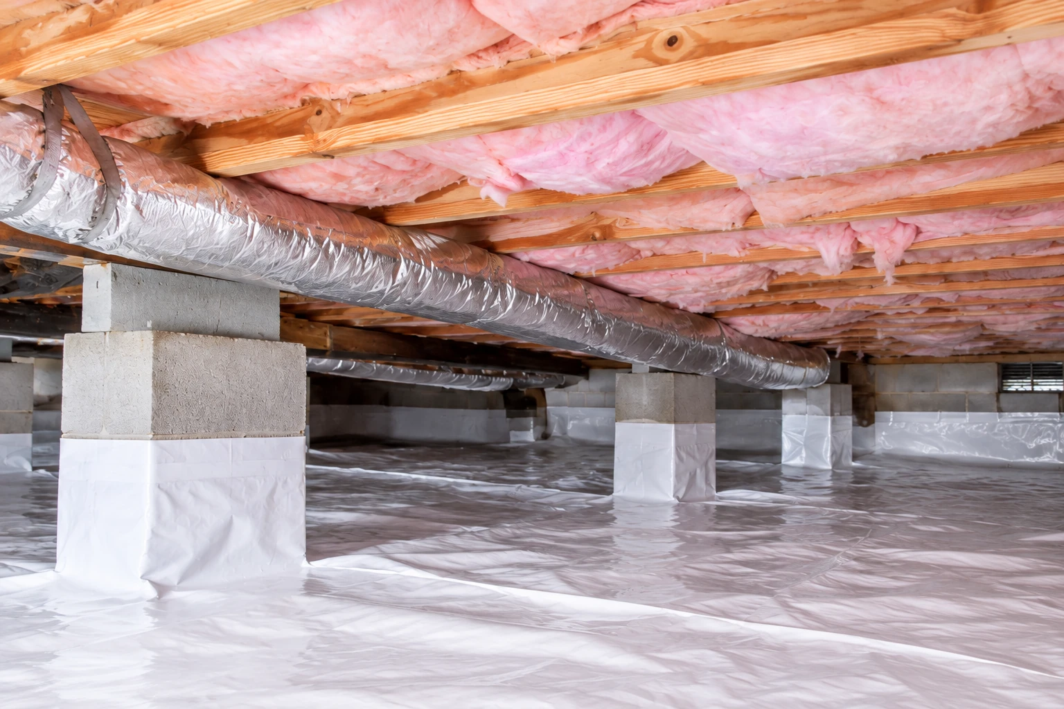A crawl space shows white plastic vapor barrier across the floor and around support piers, beneath joists filled with pink insulation.