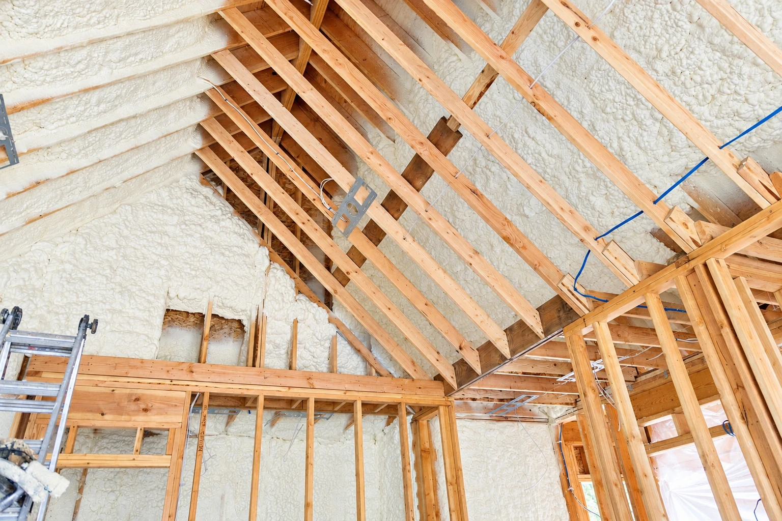 Exposed wooden roof framing and wall studs are covered with white spray foam insulation.